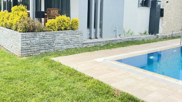Une maison moderne dotée d’une piscine, d’un patio couvert et d’un mur de soutènement en pierre.