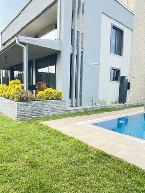 Una casa moderna con piscina, un porche cubierto y un muro de contención de piedra.