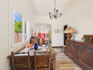 Ein Essbereich mit Holztisch, Stühlen, einer Chandelüster und Blick durch ein Fenster.