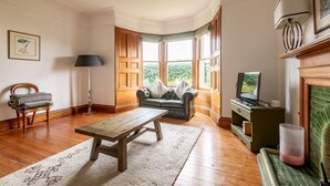 Una habitación con piso de madera, un sofá, una mesa, una lámpara, un televisor y una chimenea.