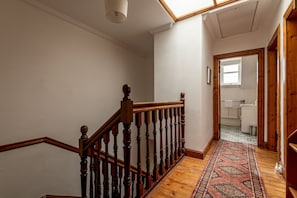 Eine Holzt Treppe mit einem gemusterten Teppich führt zu einem Badezimmer mit einer weißen Badewanne und einem Fenster.