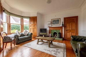 A living room with a fireplace, a sofa, a television, and a wooden coffee table. - Woodburn Terrace (No 8) | St Andrews (St Andrews)
