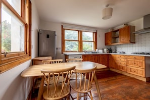 Eine Küche mit Holzausstattung, einem Kühlschrank, einem Esstisch mit Stühlen und großen Fenstern.