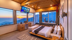 A modern hotel room with a large bed, a desk, a TV, and a view of the mountains. - Highlanders Cafe Stay (Mussoorie)