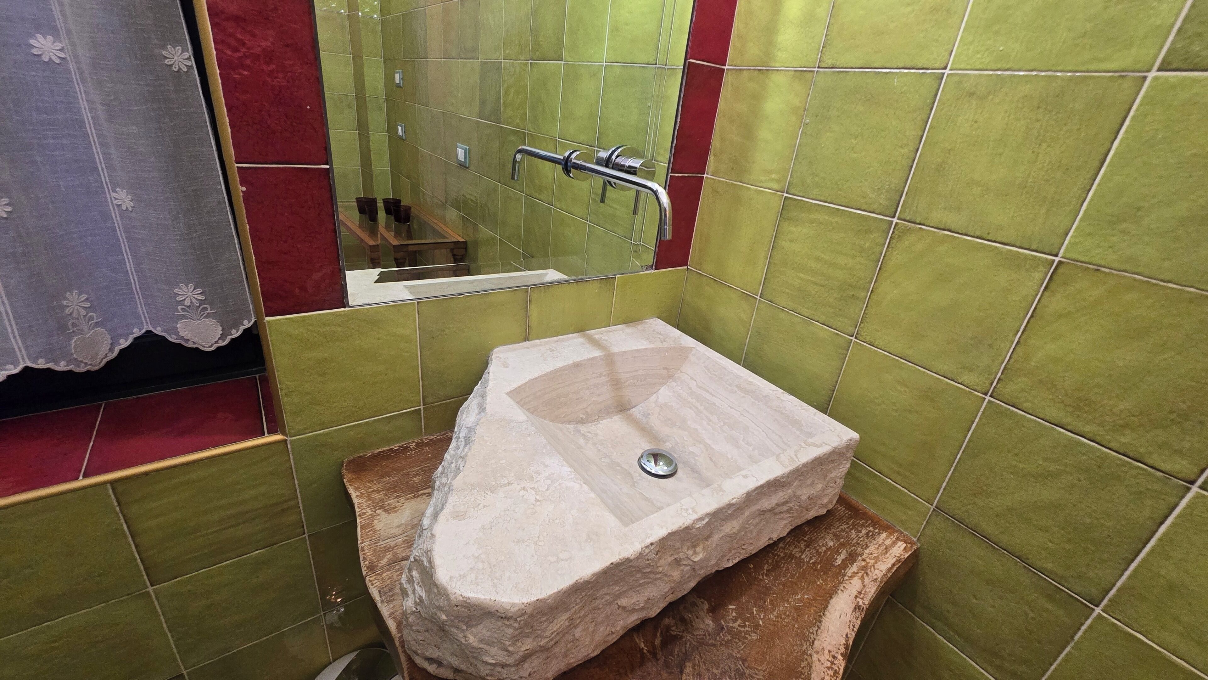 Un baño con lavamanos de piedra, paredes con azulejos verdes y un espejo.