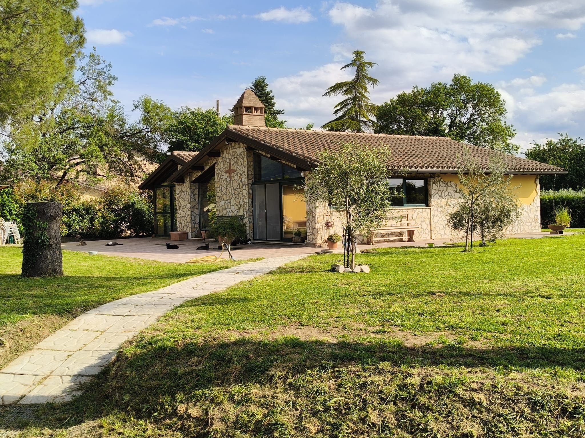 A stone building with a tiled roof, a paved entrance, and a grassy lawn.