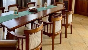 Uma sala de jantar com uma mesa de madeira comprida, seis cadeiras, um ventilador de teto e um espelho grande na parede.
