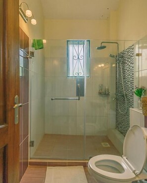 A glass-enclosed shower with a glass door, a toilet, and a small window. - Villa Macheo (Mombasa)