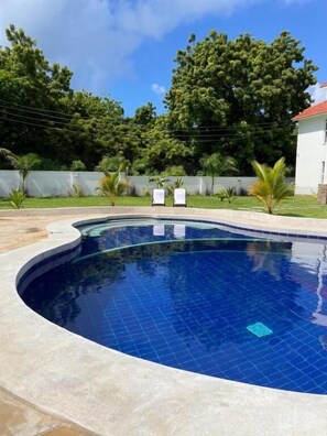 A swimming pool with a curved edge, surrounded by a concrete deck and a low wall. - Villa Macheo (Mombasa)