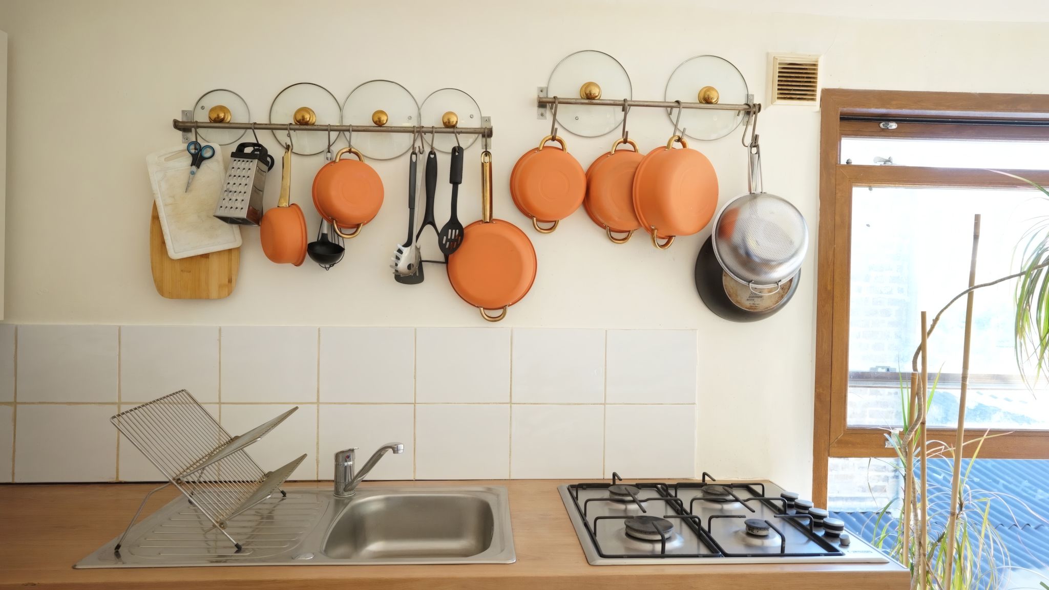 A kitchen with a stainless steel sink, a gas stove, and pots and pans hanging on a wall-mounted rack.
