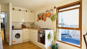 A compact kitchen with a washing machine, oven, and a window with a view of a brick building. - Cosy 1BDR Flat in Nunhead by Peckham Rye Park (Greater London)