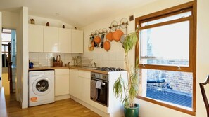A compact kitchen with a washing machine, oven, and a window with a view of a brick building. - Cosy 1BDR Flat in Nunhead by Peckham Rye Park (Greater London)
