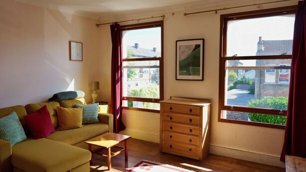 A room with a sofa, a wooden dresser, and a window with a view of buildings. - Cosy 1BDR Flat in Nunhead by Peckham Rye Park (Greater London)