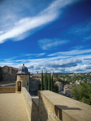 Un muro de piedra con una pequeña torre, un edificio con cúpula y un pueblo al fondo bajo un cielo azul con nubes.