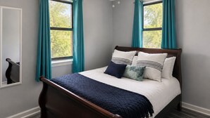 Ein Schlafzimmer mit einem Bett, türkisfarbenen Vorhängen, einem Deckenventilator und einem Fenster.