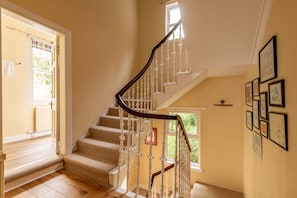 A staircase with a wooden handrail and white balusters, leading to a landing with a door and a window. - Westburn Court | St Andrews (St Andrews)