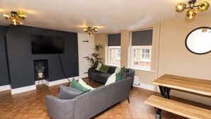 A living room with a grey sofa, a wooden bench, a TV mounted on the wall, and a window with blinds. - G's Loft (Whitby)