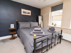 Ein Schlafzimmer mit Bett, Fenster, einem Bild an der Wand und einem kleinen Tisch.