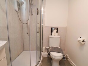 Ein Badezimmer mit einer Duschkabine, einer Toilette mit Handtuch und einer Toilettenpapierrolle an der Wand.