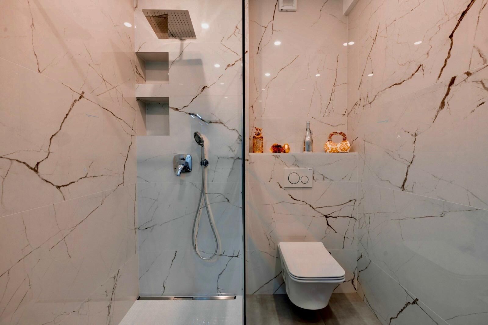 Een moderne badkamer met een douchecabine van glas, een toilet en marmeren wanden.