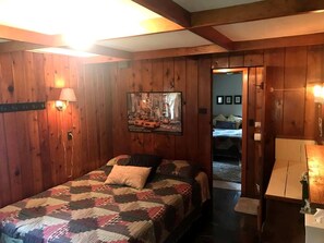 Een kamer met houten lambrisering, een bed, een schilderij en een deur die naar een andere kamer leidt.