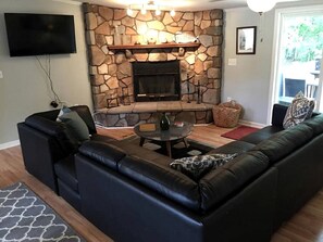 Una sala de estar con chimenea de piedra, sofá de cuero negro y televisor de pantalla plana.
