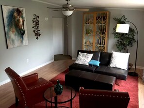 Ein Wohnzimmer mit einer Couch, einem roten Sessel, einem Couchtisch, einem Deckenventilator und einem Gemälde an der Wand.