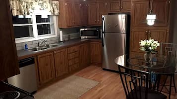 A kitchen with wooden cabinets, a stainless steel refrigerator, a microwave, and a glass dining table with chairs.