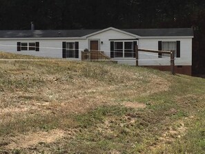 A single-story mobile home with a front porch, a small attached garage, and a grassy yard.