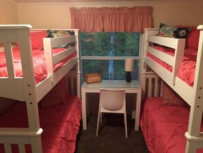 A bunk bed room with a desk and chair, a window with a view of trees, and a pink curtain.