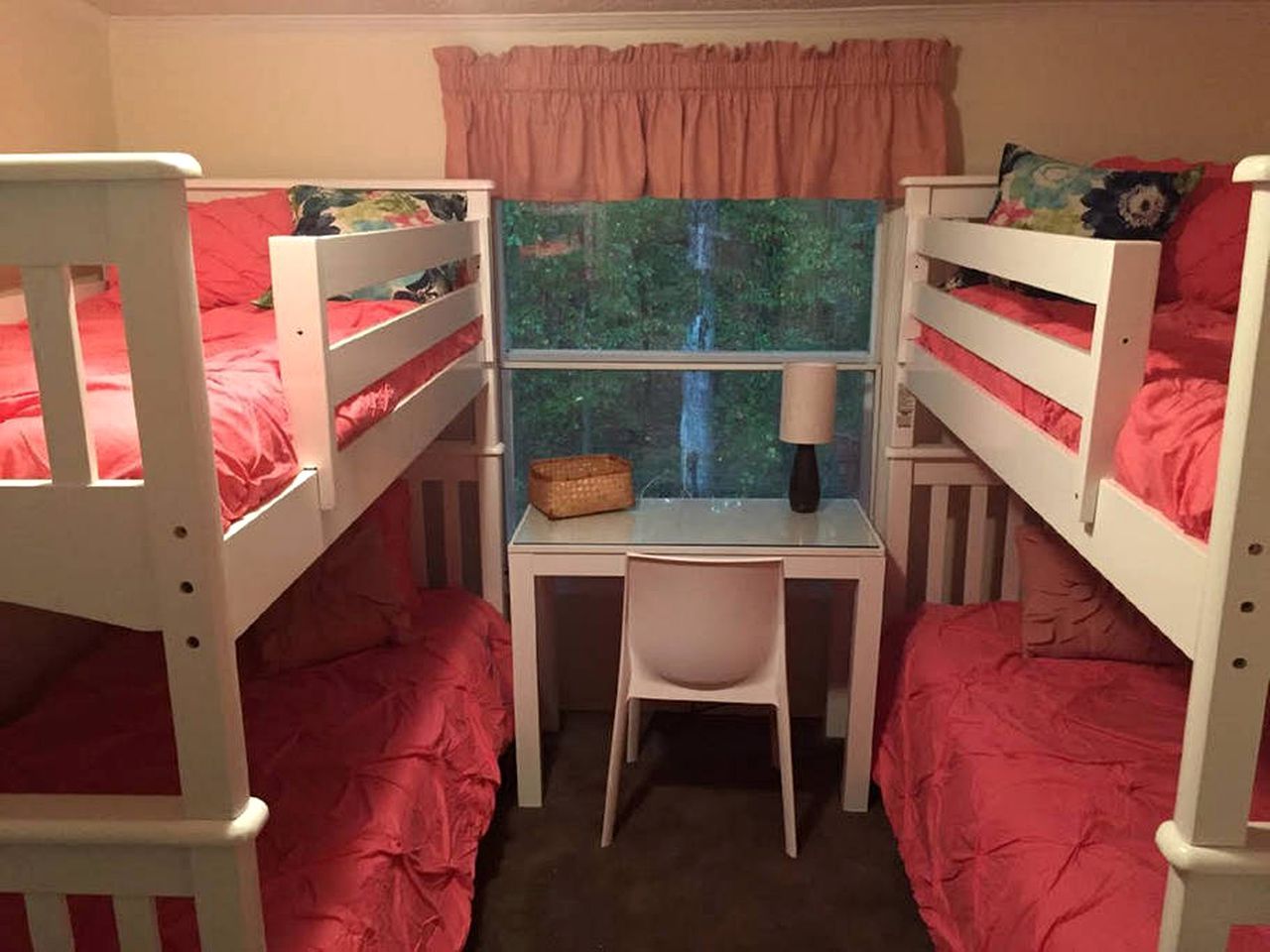 Une chambre avec un lit superposé, un bureau et une chaise, une fenêtre donnant sur des arbres et un rideau rose.