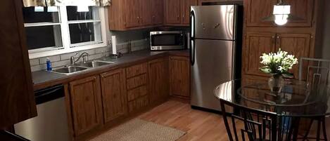 Una cocina con armarios de madera, un refrigerador de acero inoxidable, un microondas y una mesa de comedor de vidrio con sillas.