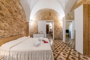 Quarto de hotel com parede de pedra, cama de madeira, espelho e chão com padrão.