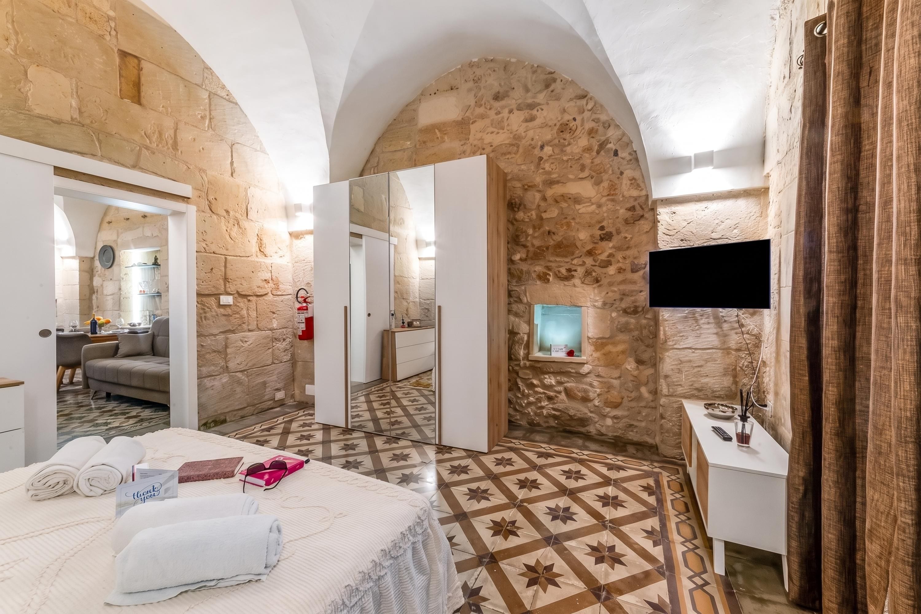Une chambre d’hôtel avec des murs en pierre, un lit avec des serviettes, une télévision et une salle de bain avec un miroir.