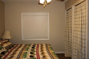 Une chambre à coucher avec un lit, une fenêtre avec des stores, une lampe et un rideau.