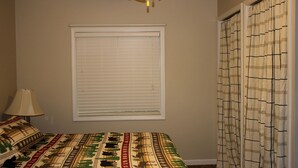 Un dormitorio con cama, ventana con persianas, lámpara y cortina.