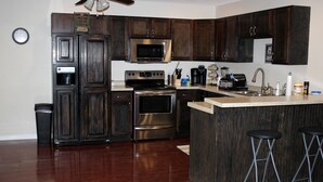 Una cocina moderna con armarios de madera oscura, electrodomésticos de acero inoxidable, microondas, horno y una zona de bar con taburetes.