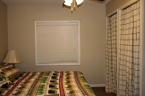 A bedroom with a bed, a window with blinds, a lamp, and a curtain. - Beautiful Cabin near the Cedar River for a Perfect Family Vacation in Letts, Iowa (Letts)