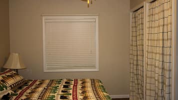 A bedroom with a bed, a window with blinds, a lamp, and a curtain.