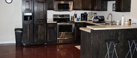 A modern kitchen with dark wood cabinets, stainless steel appliances, a microwave, oven, and a bar area with stools.