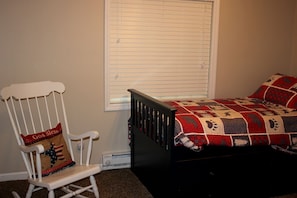 A bedroom with a bed, a rocking chair, a window with blinds, and a wall-mounted heater. - Beautiful Cabin near the Cedar River for a Perfect Family Vacation in Letts, Iowa (Letts)