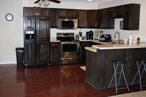 Una cocina moderna con armarios de madera oscura, electrodomésticos de acero inoxidable, microondas, horno y una zona de bar con taburetes.