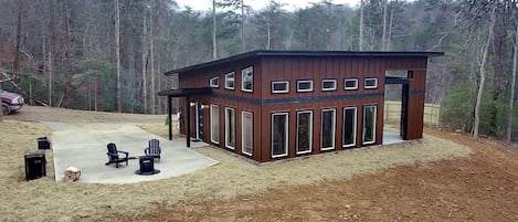 Une cabane en bois moderne dotée d’un patio, entourée d’une forêt.