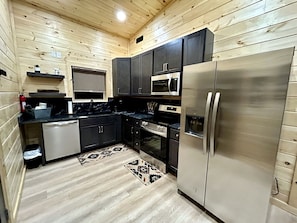 A compact kitchen with dark cabinets, stainless steel appliances, and a patterned rug. - Romantic Cabin in Shady Grove Area of the Smoky Mountains: A Perfect One-Level Retreat for Couples (Sevierville)