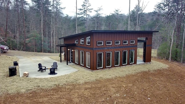 A modern wooden cabin with a patio, surrounded by a forest. - Romantic Cabin in Shady Grove Area of the Smoky Mountains: A Perfect One-Level Retreat for Couples (Sevierville)