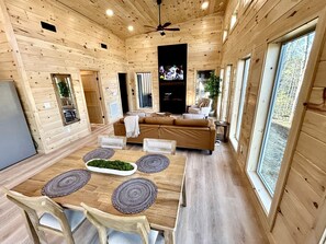 A wooden cabin interior with a dining area, sofa, TV, and large windows. - Romantic Cabin in Shady Grove Area of the Smoky Mountains: A Perfect One-Level Retreat for Couples (Sevierville)