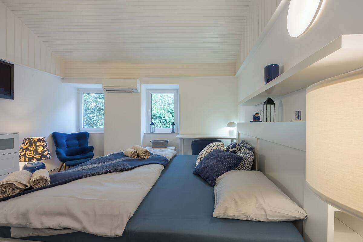 Et hotelværelse med to senge, et skrivebord, en stol og to vinduer.