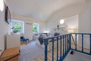 Quarto moderno com uma cama grande, uma escrivaninha e uma cadeira. Há uma janela com vista para o verde lá fora.