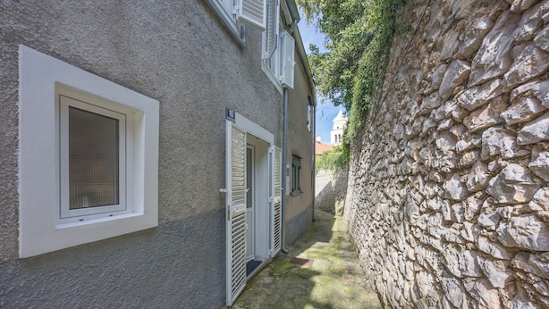 Ein schmaler Gang mit einer Steinmauer auf der einen Seite und einem Gebäude mit Fenster und Tür auf der anderen.