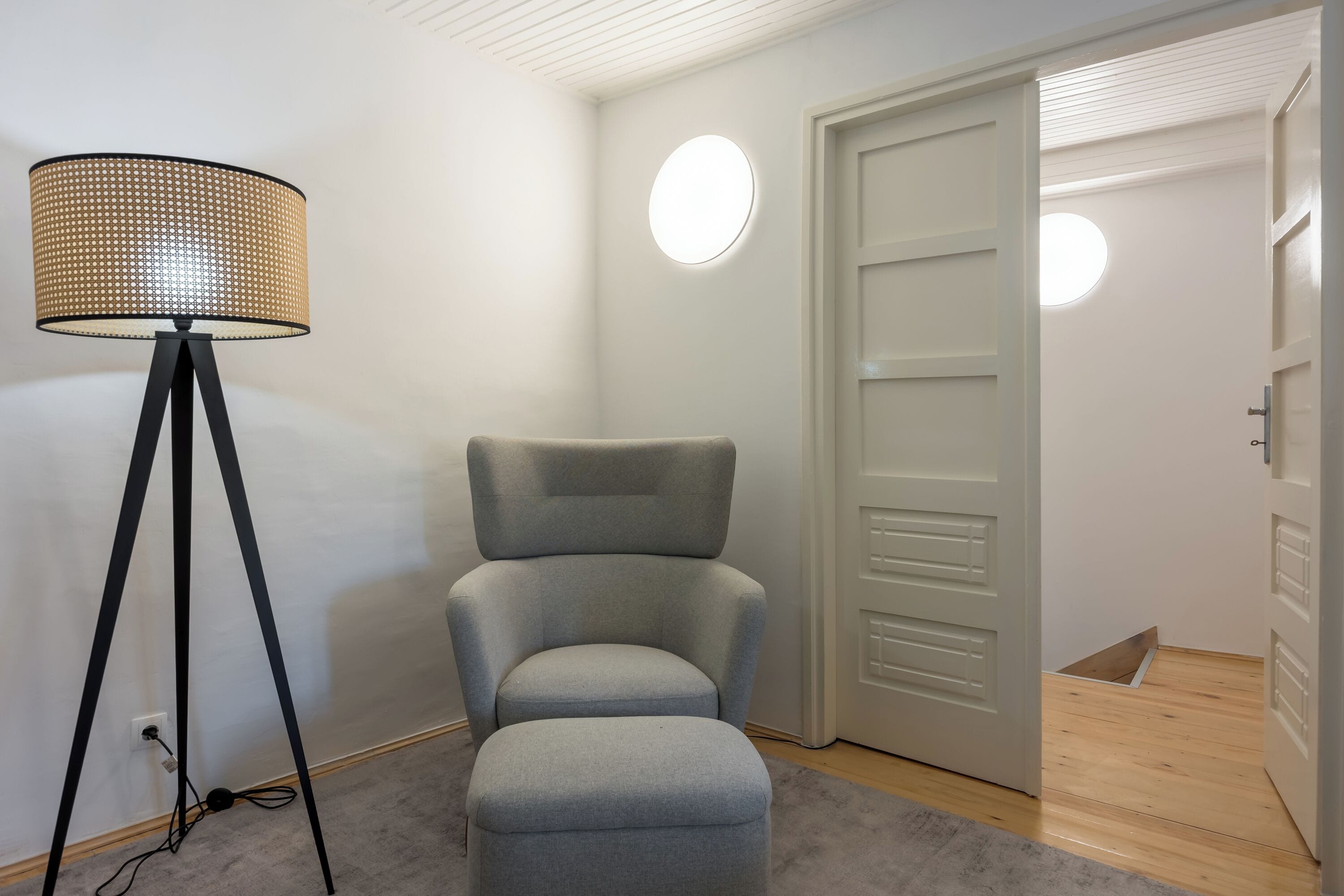 A room with a grey upholstered chair, a floor lamp, and a door with a light switch.